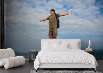 Male runner relaxing after training while standing on stone rock with hands raised against sky background with copy space area for your advertising, fit men celebrating achievement with hands raised Wall mural