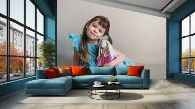 Cute little girl in blue dress looks at camera and holds her toy rabbit Wall mural