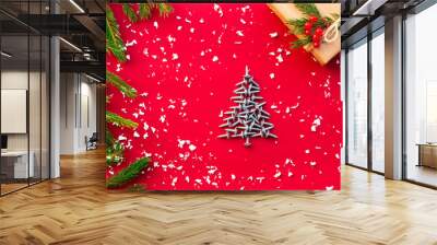 Christmas tree of screws, gift with branches of a Christmas tree and berries on a red background. Flat lay. Copy space. Wall mural