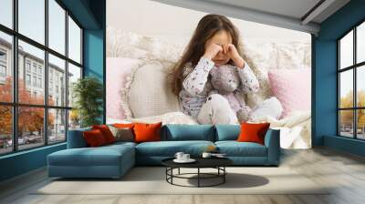 Depressed, sad, disappointed kid, girl rubbing eyes, sit with stuffed bear toy in soft white bed in the morning. Abandoned, orphan children, sadness and stress. Painful emotions and loneliness Wall mural