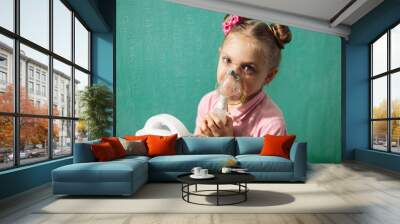 a little pretty blonde girl 5 - 6 years old in pink, breathes a compression nebulizer (inhaler) through a mask for lung disease, bronchitis and whooping cough, picture on a blue background... Wall mural