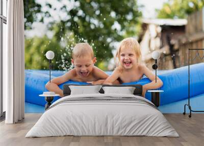 happy cute children, preschoolers, fair-haired blue-eyed brother and sister bathe in the summer in the village in the inflatable pool, make splashes and laugh joyfully Wall mural