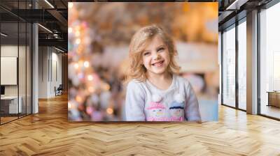 Portrait of a fair-haired beautiful curly happy smiling girl 6-7 years old in a New Year's Eve on Christmas Eve against a background of lights Wall mural