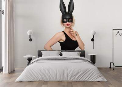 A sexy blonde woman dressed in a black Easter bunny costume and bunny ears stands on a white background and poses sensually. Halloween and Easter Bunny Costume - Hot Girl. Wall mural