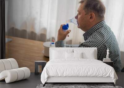 Elderly man sitting on a table and using a nebulizer mist at home Wall mural