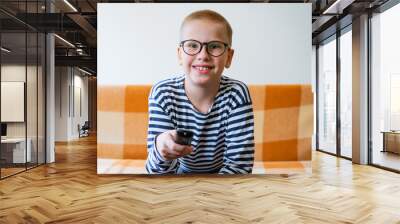 A teenage boy watches tv, using remote control to change channels. Young man is unhappy with what he sees on the tv screen. Sitting on the sofa in the living room at home in casual clothes Wall mural