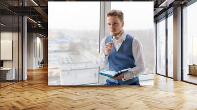 Thoughtful business man with beard in shirt and vest with notepad in his hand writes notes and thinks over a plan for doing business in his work office. Reflections and ideas are written in a diary Wall mural