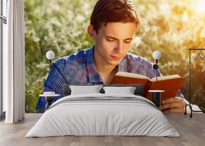 young man sitting in nature reading a book Wall mural