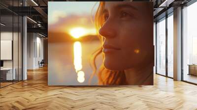 A close-up of a woman by a lake at sunset, her face filling the frame with vibrant colors of the sunset in soft focus behind her, warm light illuminating her features.  Wall mural