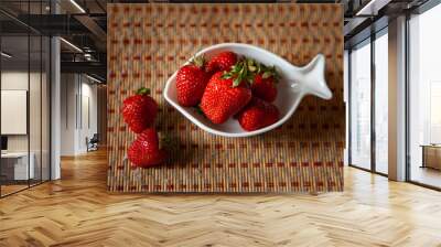 five large red strawberries in a white deep fish-shaped plate and two strawberries lying side by side against a light brown vertical striped litter. summer time. large horizontal photo. background. Wall mural