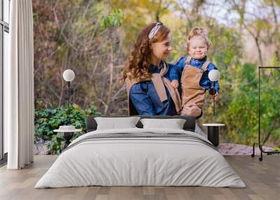 happy mother and her young daughter toddler enjoying day outdoors beautiful autumn forest. mother holding her daughter. smiling looking at the camera. stylish in family look clothes  Wall mural