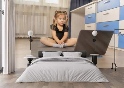 4 years old girl practices yoga in front of a laptop at home, sunlight, backlight. online gymnastics classes Wall mural