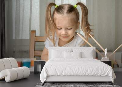 a girl with pigtails sits on a chair and paints the sun with a brush with yellow paint, age 3-4 years Wall mural