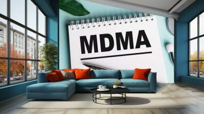 In a white notebook on a blue background, near a sheet of shefflers, a stethoscope, a syringe and an electronic thermometer, the word MDMA is written. Medical concept Wall mural