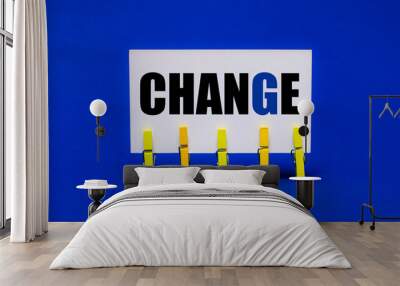 On a bright blue background on yellow clothespins, a white card with the text CHANGE Wall mural