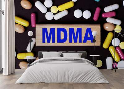 On a dark background, multi-colored pills and the word MDMA on a wooden block. Medical concept Wall mural