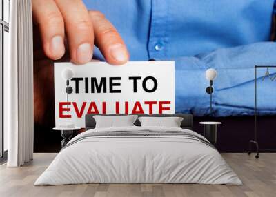 TIME TO EVALUATE is written on a white business card in a man's hand. Advertising concept Wall mural