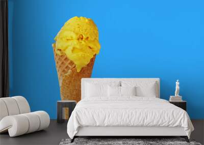 Mango yellow ice cream in a waffle cone on a light blue background. Close-up Wall mural