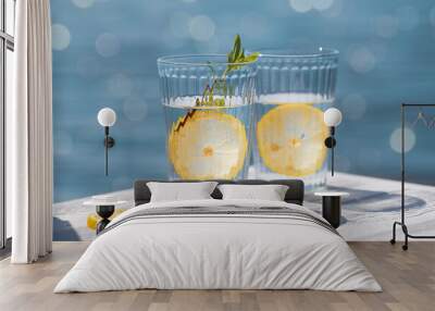 Two glasses of mineral water with lemon on a white table against the background of a blurred blue sea with bokeh light. Wall mural