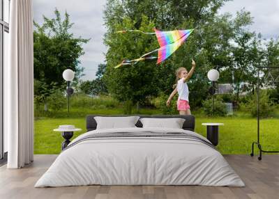 cheerful happy little girl is flying a rainbow kite. kids summer fun. summer vacation for kids. childhood holiday concept Wall mural