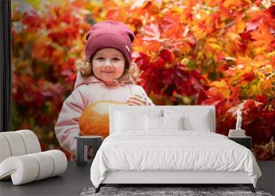 happy little cute girl carrying, holding, collecting orange pumpkin. smiling kid harvesting in autumn on red maple background. child preparing for thanksgiving day, halloween holiday in october. Wall mural