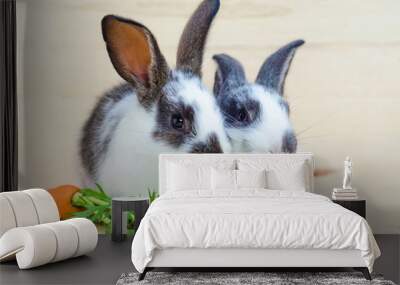 two little rabbits eating fresh vegetables, carrot, leaves on wooden background.  feeding the rodent with a balanced diet, food. bunny is a Easter symbol. closeup Wall mural