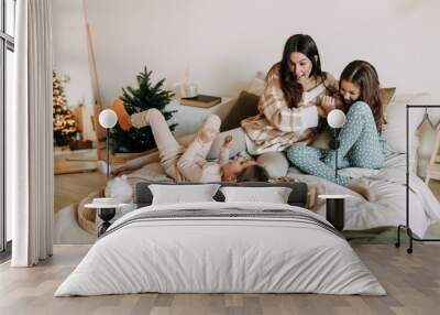 A happy mom with two daughters is resting, relaxing and having fun sitting on the bed in a cozy decorated bedroom during the Christmas holiday at home during the New Year vacations. Selective focus Wall mural