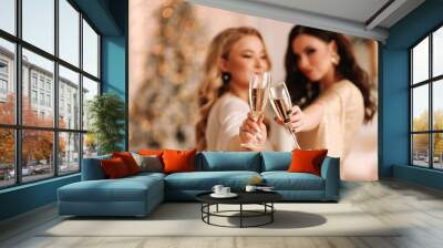 Beautiful young women girlfriends with hair and makeup in fashionable elegant outfits hold glasses of champagne drink alcohol celebrate the New Year holiday and Christmas at home. Selective focus Wall mural