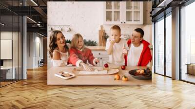 The concept of Christmas. A family with two children in sweaters prepare a festive food in the decorated kitchen in the house on a holiday. Two parents with their daughter and son have fun at home Wall mural