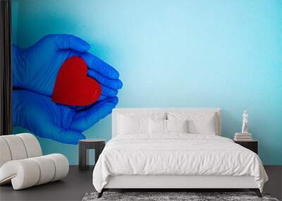 red heart in hands in blue medical gloves on a blue background. background for the day of the medic, top view, space for text Wall mural