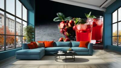 A refreshing summer drink made from strawberries and mint, juice, soda with ice cubes and berry slices, in a beautiful glass with water droplets on a wooden board, dark background with place for text Wall mural