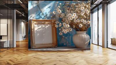 A photo frame placed next to a vase filled with small white flowers, creating a charming and elegant setup. The frame is simple and stylish, while the vase holds a delicate arrangement of white blosso Wall mural