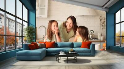 Young happy beautiful family having breakfast together at home. mother and two cute little kids eating healthy food in morning, talking and smiling while standing in modern kitchen Wall mural