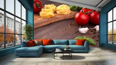 Raw tagliatelle pasta with fresh basil, garlic and branch of tomatoes on rustic wooden table Wall mural