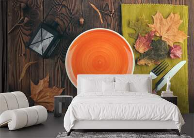 Top view with empty orange plate ready to place food, cutlery, colored leaves, candlestick lantern on rustic wooden table. Autumn table with copy space Wall mural