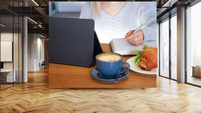 Close up woman in casual clothes sitting and browsing laptop at kitchen table with cup of coffee and plate of croissant Wall mural