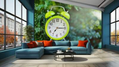 Green alarm clock in the green foliage in nature, shows 7 o'clock in the morning. Early morning concept. Wall mural