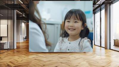 A young asian girl is sitting in a dentist's chair with a smile on her face Wall mural