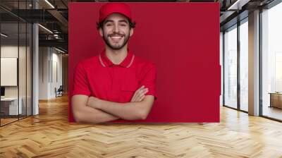 Smiling young man in a red uniform and cap with arms crossed Wall mural