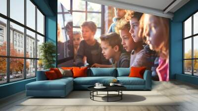 A group of children gathered around a large computer screen, intensely watching as their teacher demonstrates coding principles. Sunlight streams through nearby windows, casting so Wall mural