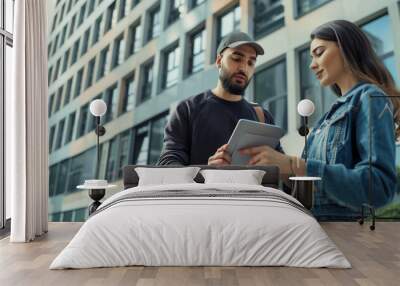 of a deliveryman using a digital tablet to confirm the receipt of a parcel with a female recipient in front of an office building, illustrating professional service, courier delive Wall mural