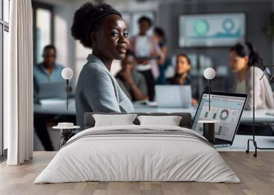 of an African businesswoman confidently presenting financial forecasts on her laptop to invisible stakeholders, with colleagues collaborating on related projects in the background, Wall mural