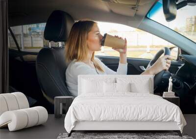 Beautiful blonde woman drinking coffee in car while commuting to work Wall mural