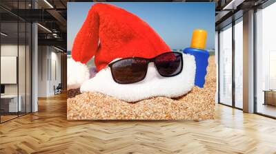 Closeup image of Santa's hat with sunglasses and sun lotion on sandy sea beach. Concept of travel and tourism on Christmas, New Year and winter holidays. Wall mural