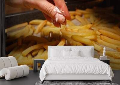 Closeup of female hand pouring salt on frying french fries potatoes on baking pan. Fast food, healthy nutrition, cooking in oven. Wall mural