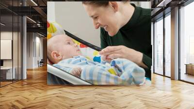 Portrait of smiling mother looking at her cute baby son sitting in electric rocking chair. Child development and happy parenting Wall mural