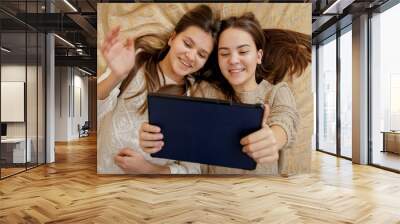 Top view of two girls lying on bed and using tablet computer. Remote studying and communication from home Wall mural