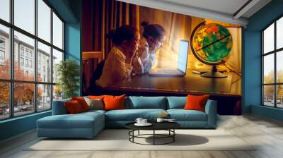 Two little girls looking with amazement at laptop at night Wall mural