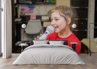 A child sings into a microphone in his room. Portrait of a girl singing a song. Wall mural