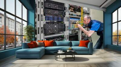 A man commutes wires in a server room. A technician works with server equipment in a data center. Wall mural